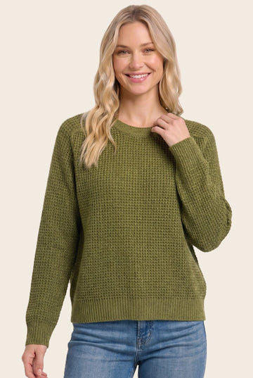 woman wearing a green textured knit sweater and smiling, paired with blue jeans