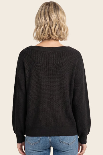 woman wearing a black oversized sweater with a textured knit and long sleeves, viewed from the back