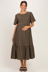 woman wearing a brown and black checkered maternity dress with short sleeves and a tiered skirt, holding her baby bump