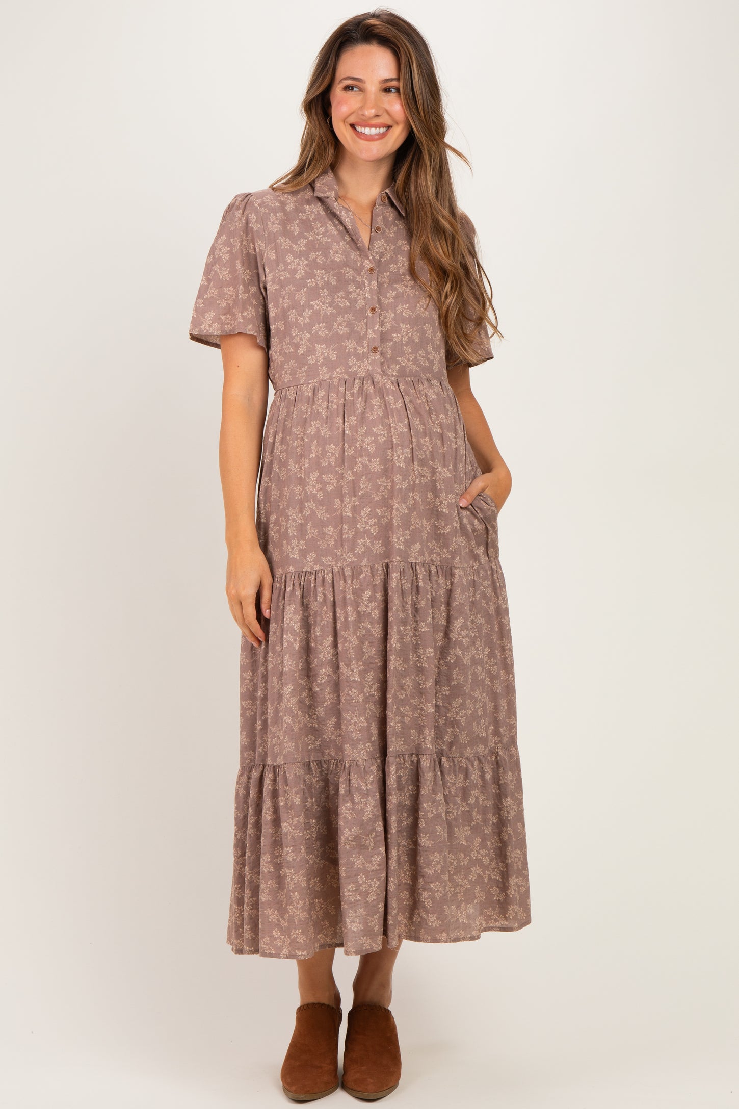woman wearing a mauve maternity dress with short sleeves, button front, and tiered design, showing a baby bump