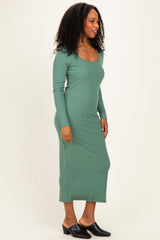 woman wearing a fitted long sleeve green midi dress with a scoop neckline and side slit, styled with black mules