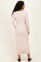 woman wearing a long sleeve light pink maternity maxi dress with a fitted silhouette, showing a baby bump from behind