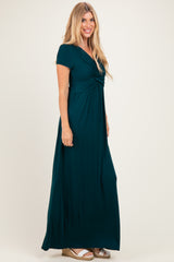 woman wearing a teal maxi dress with short sleeves and a gathered bodice, standing sideways with a neutral background