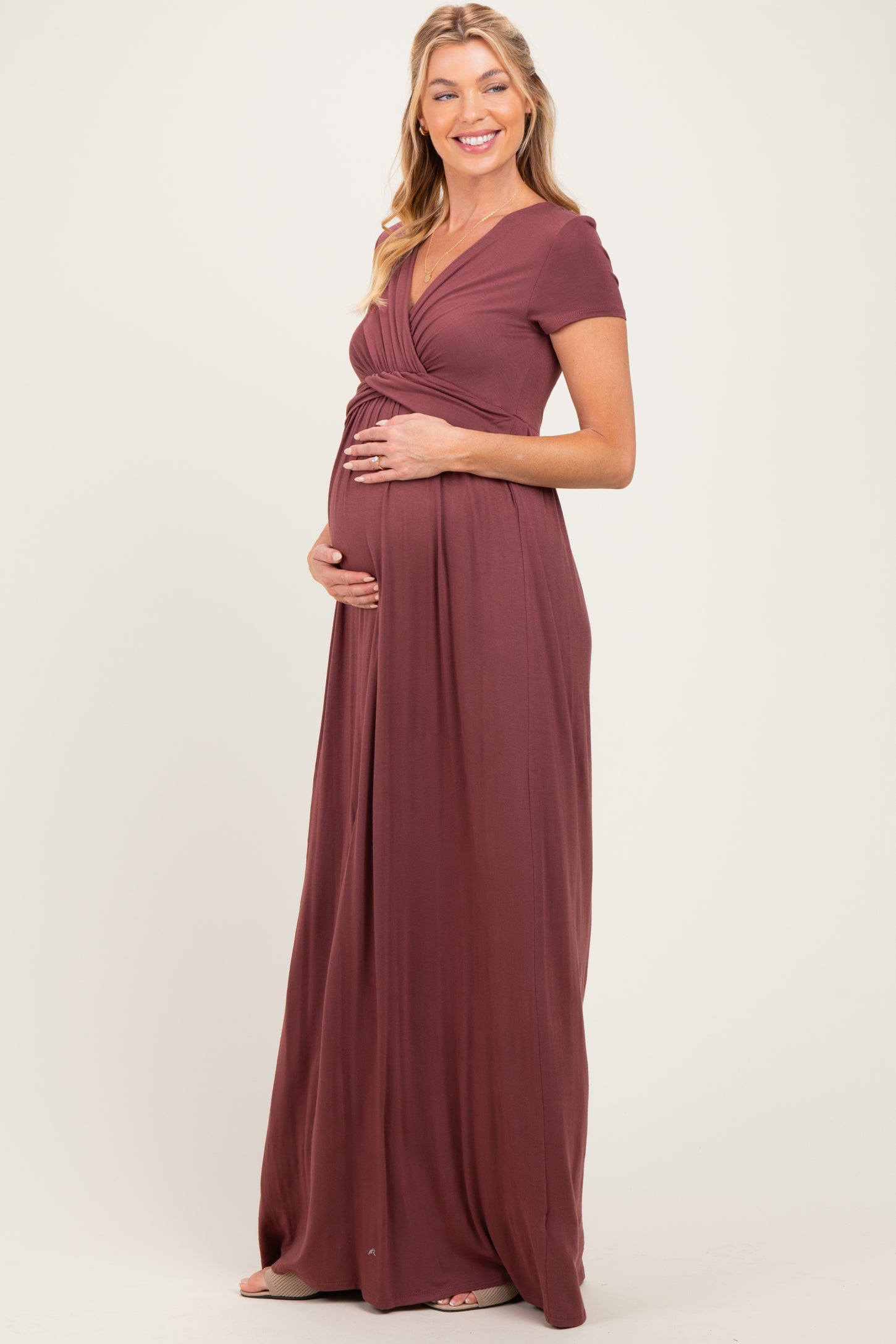 woman wearing a burgundy maternity maxi dress with a v-neck and short sleeves, holding her baby bump