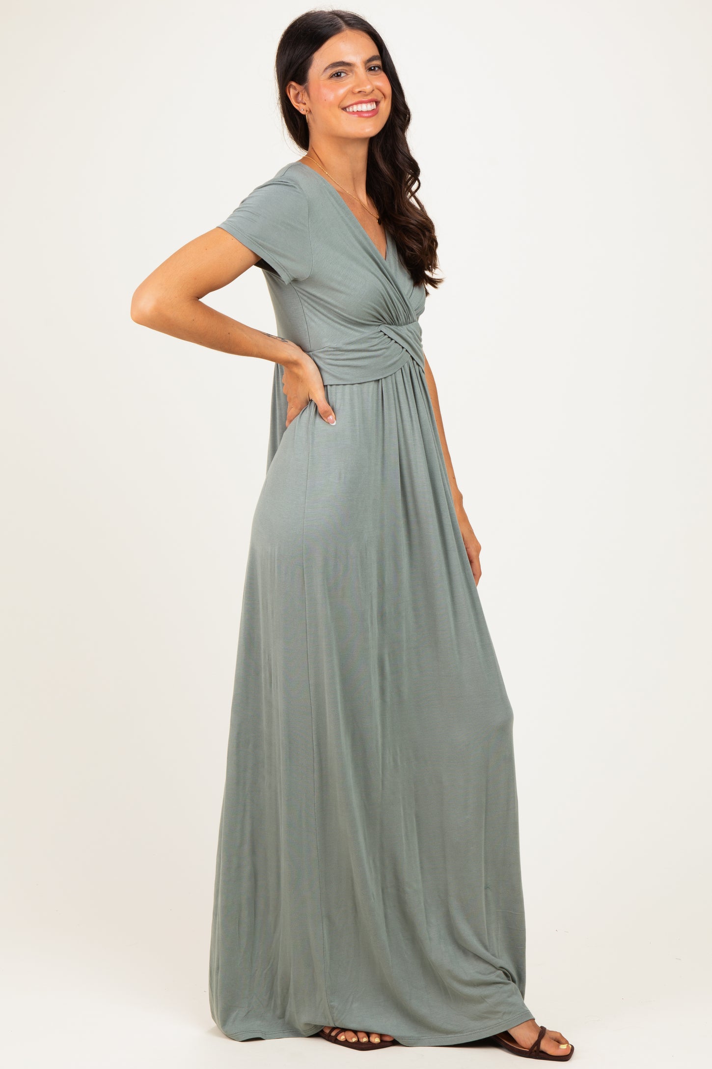 woman wearing a sage green maxi dress with a v-neck and short sleeves, posing with one hand on her hip