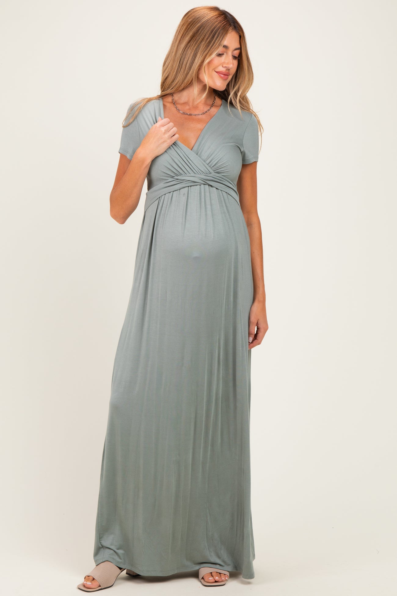 woman wearing a sage green short sleeve maternity maxi dress with a v-neck and a visible baby bump