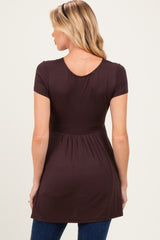 woman wearing a dark brown short sleeve maternity top with a slightly flared hem and gathered waist.