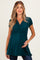 woman wearing a teal maternity top with a wrap style and short sleeves, holding her baby bump