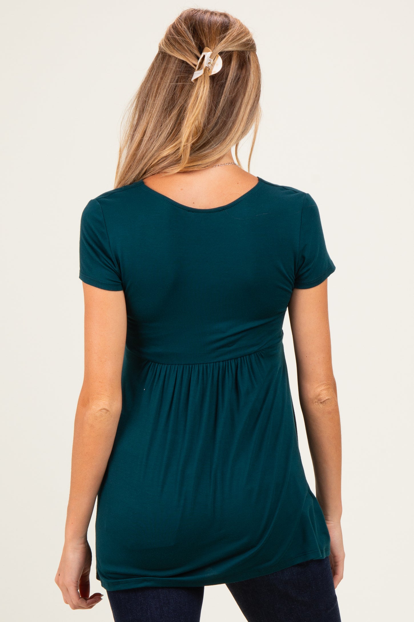 woman wearing a dark teal maternity top with a gathered waist and short sleeves, showing a relaxed fit