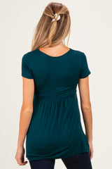 woman wearing a dark teal maternity top with a gathered waist and short sleeves, showing a relaxed fit