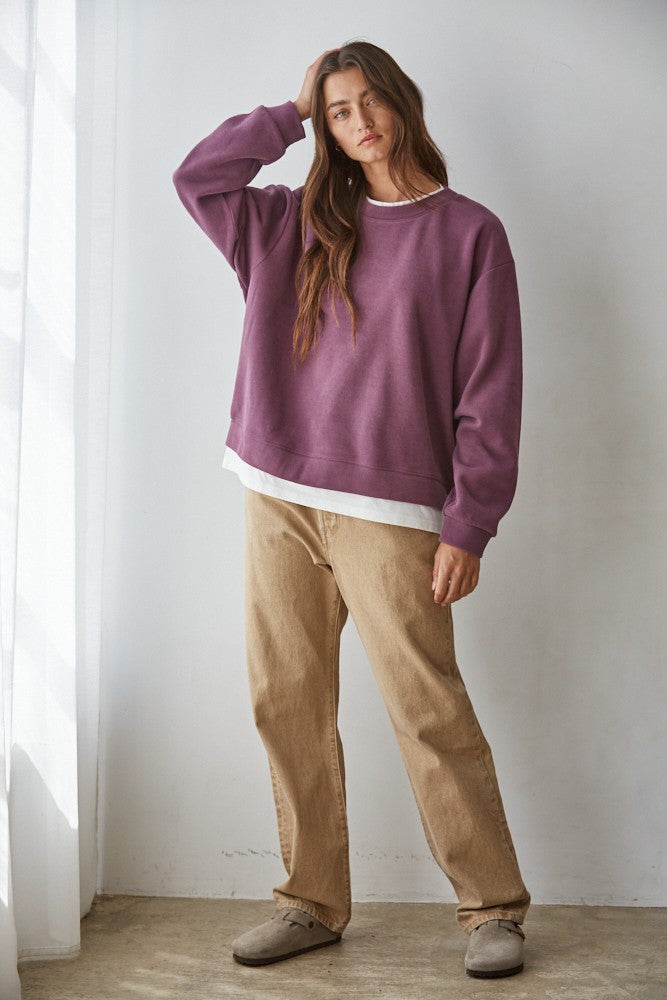 woman wearing a purple oversized sweatshirt layered over a white shirt and paired with beige wide-leg pants