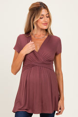 woman wearing a burgundy short sleeve maternity top with a draped v-neck and gathers at the bust, showing a baby bump