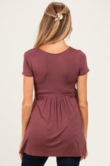 woman wearing a burgundy short sleeve maternity top with a flared waist and back pleat detail