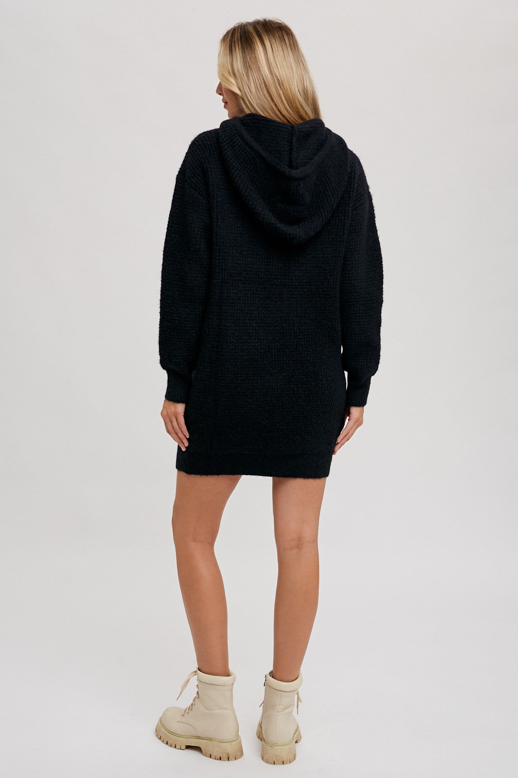 woman wearing a black hooded sweater dress with long sleeves and a relaxed fit, paired with beige ankle boots