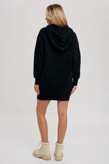 woman wearing a black hooded sweater dress with long sleeves and a relaxed fit, paired with beige ankle boots