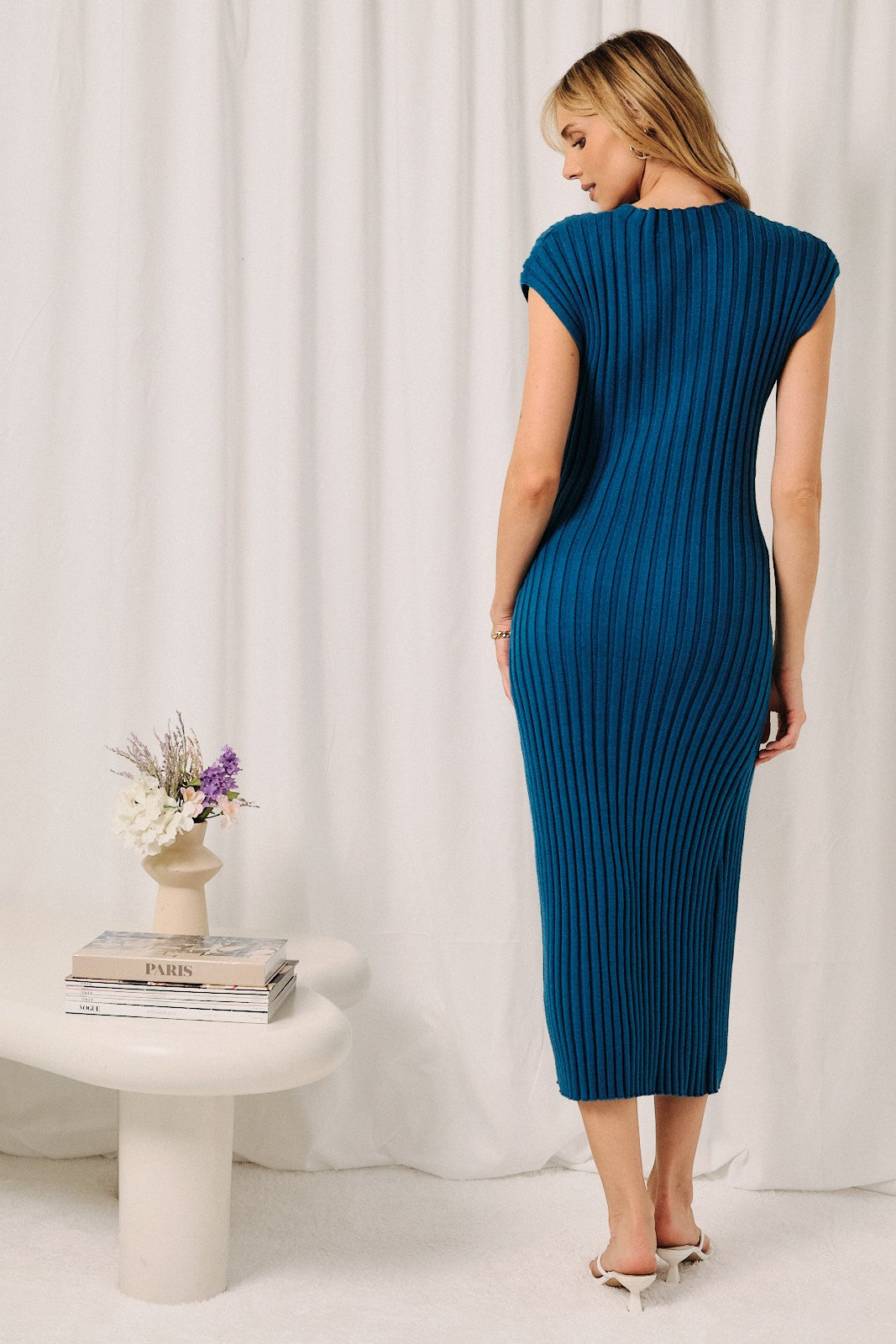 woman wearing a teal ribbed midi dress with cap sleeves, standing with her back to the camera