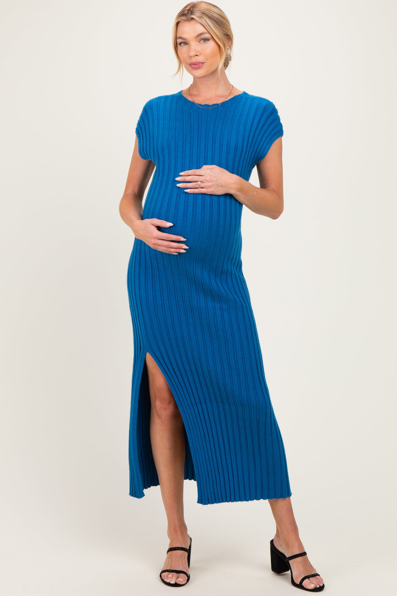 woman wearing a blue ribbed maternity dress with a side slit and holding her baby bump