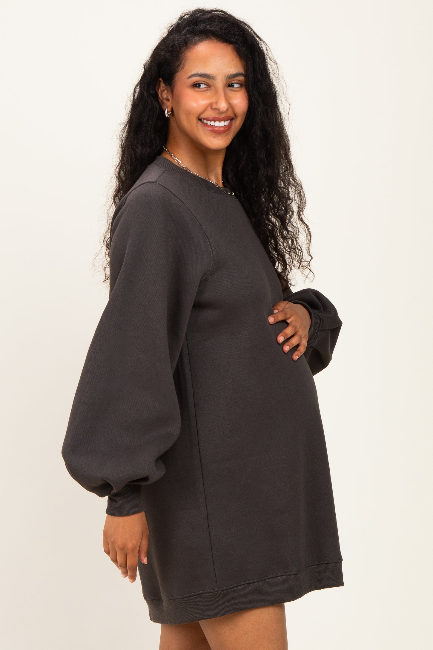 woman wearing a dark gray maternity sweatshirt dress with puff sleeves and holding her baby bump