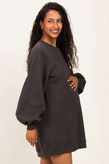 woman wearing a dark gray maternity sweatshirt dress with puff sleeves and holding her baby bump