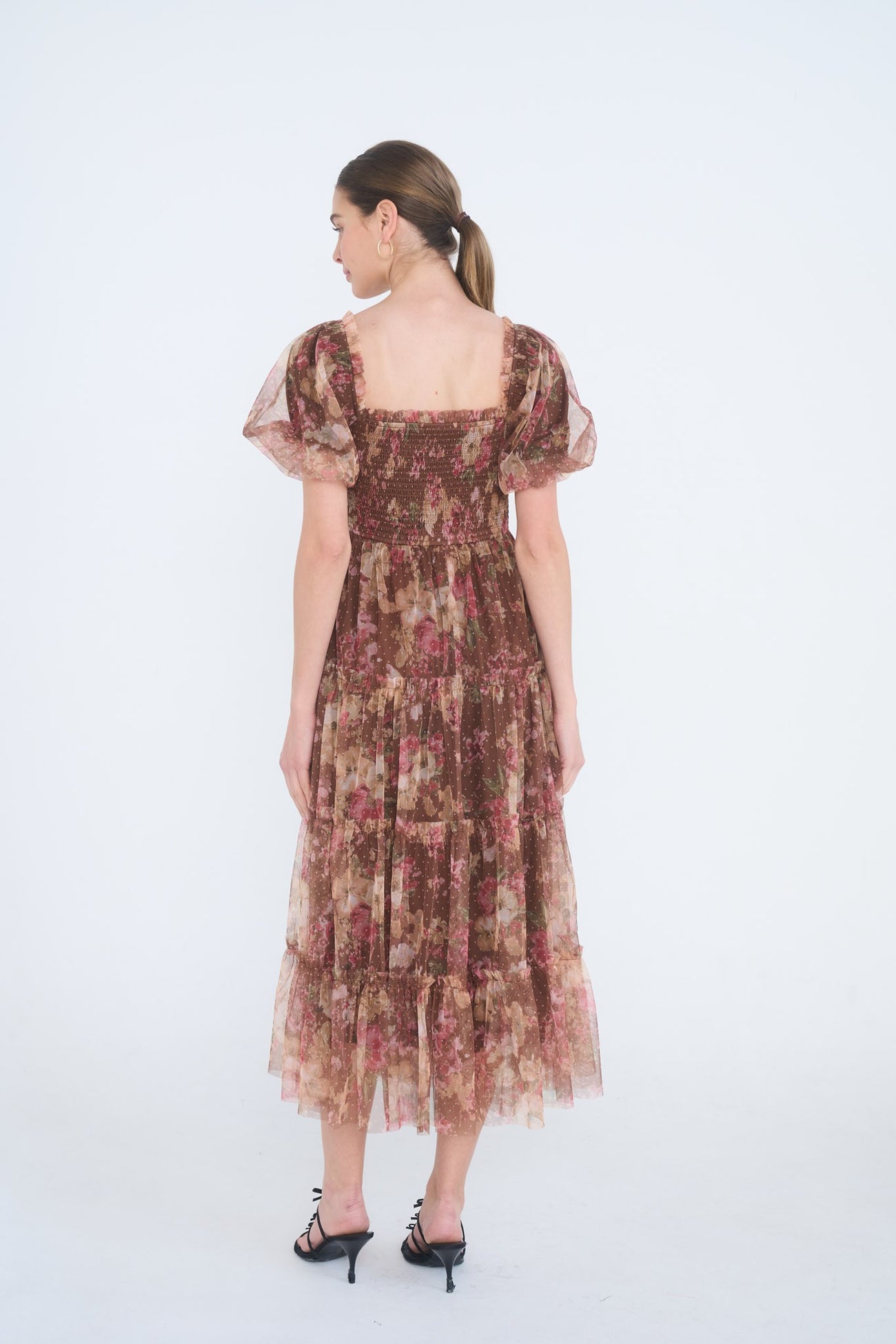 woman wearing a brown floral midi dress with puff sleeves and tiered ruffle hem, shown from the back