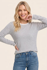 woman wearing a light gray and white striped long sleeve top with a relaxed fit and smiling at the camera