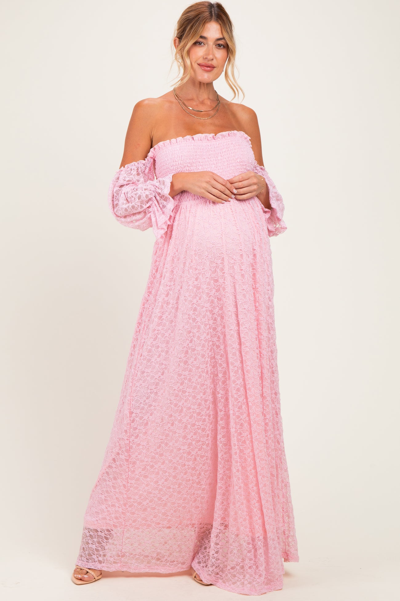 woman wearing a pink off-the-shoulder maternity dress with lace details and a visible baby bump