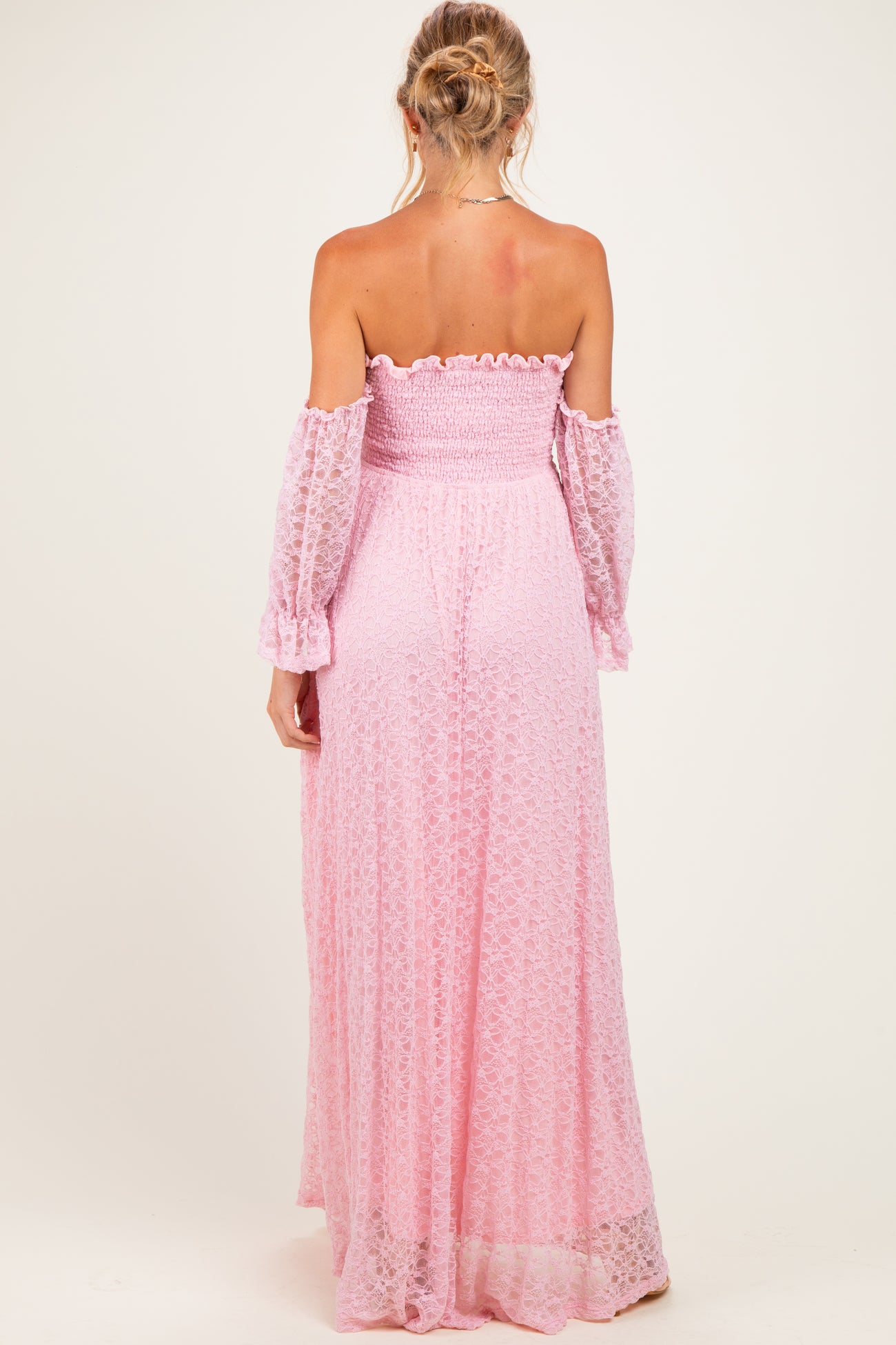 woman wearing a light pink off-the-shoulder maternity maxi dress with long, flowing sleeves and a smocked bodice, showing her back