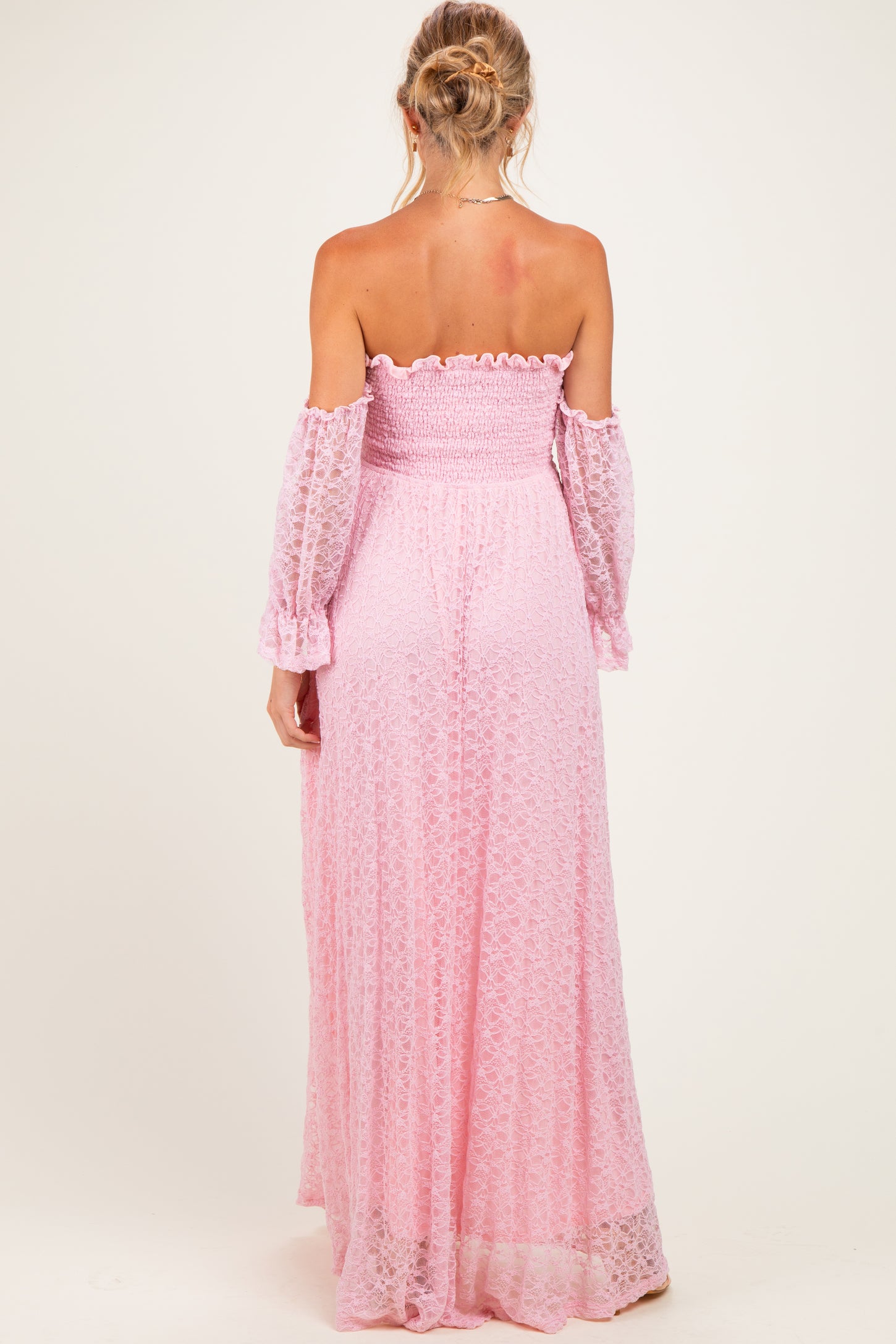 woman wearing a light pink off-the-shoulder maternity maxi dress with long, flowing sleeves and a smocked bodice, showing her back