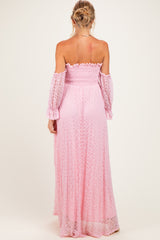woman wearing a light pink off-the-shoulder maternity maxi dress with long, flowing sleeves and a smocked bodice, showing her back