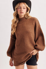 woman wearing a brown oversized sweater with balloon sleeves and side slits, paired with black shorts and a wide-brimmed hat