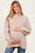 woman wearing a beige oversized maternity sweater with a high neck and holding her baby bump