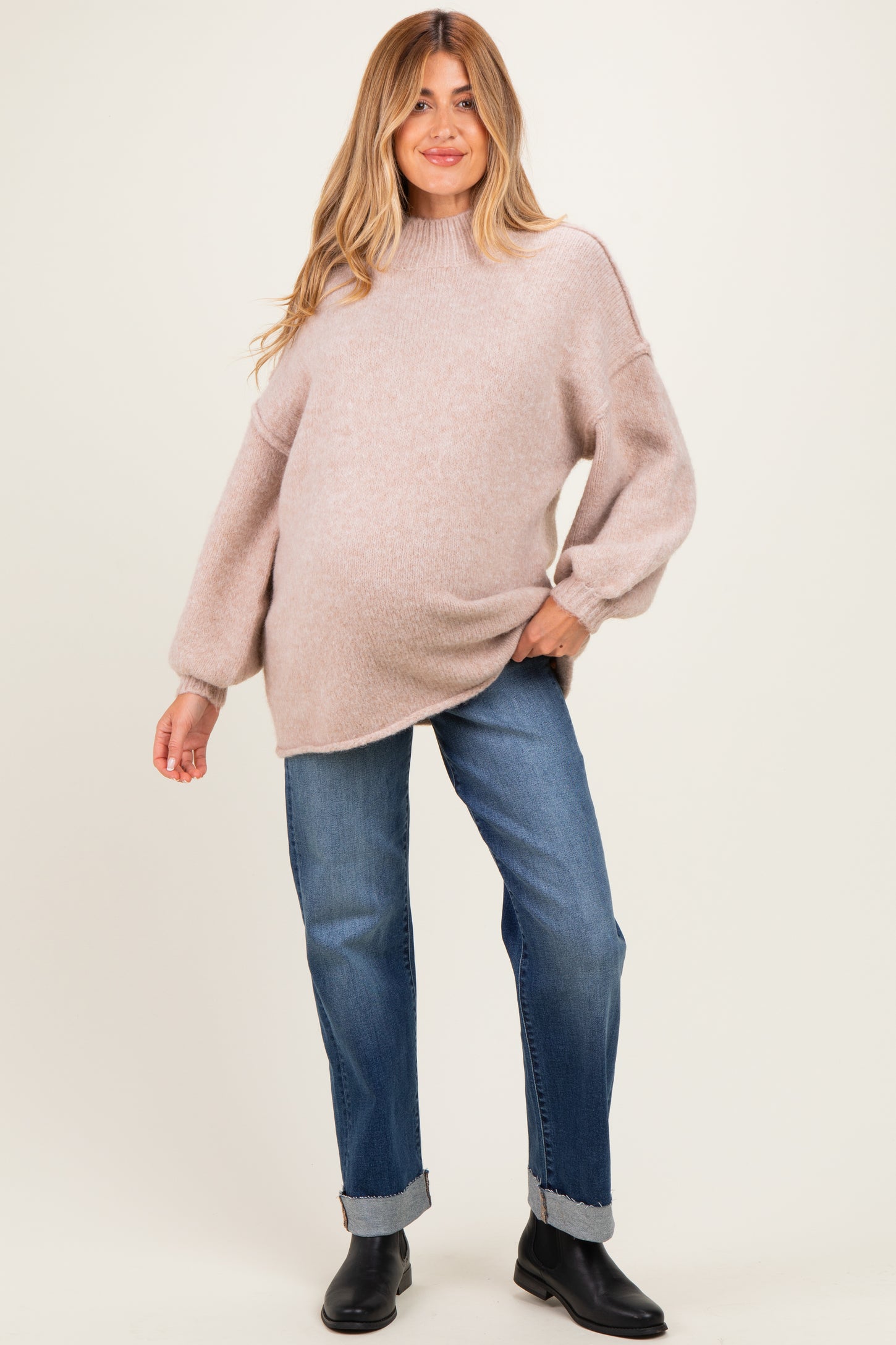 woman wearing a light pink oversized maternity sweater and blue jeans with a visible baby bump