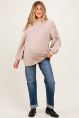 woman wearing a light pink oversized maternity sweater and blue jeans with a visible baby bump