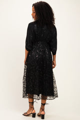 woman wearing a black sheer midi dress with floral embroidery and a cinched waist, showing the back view