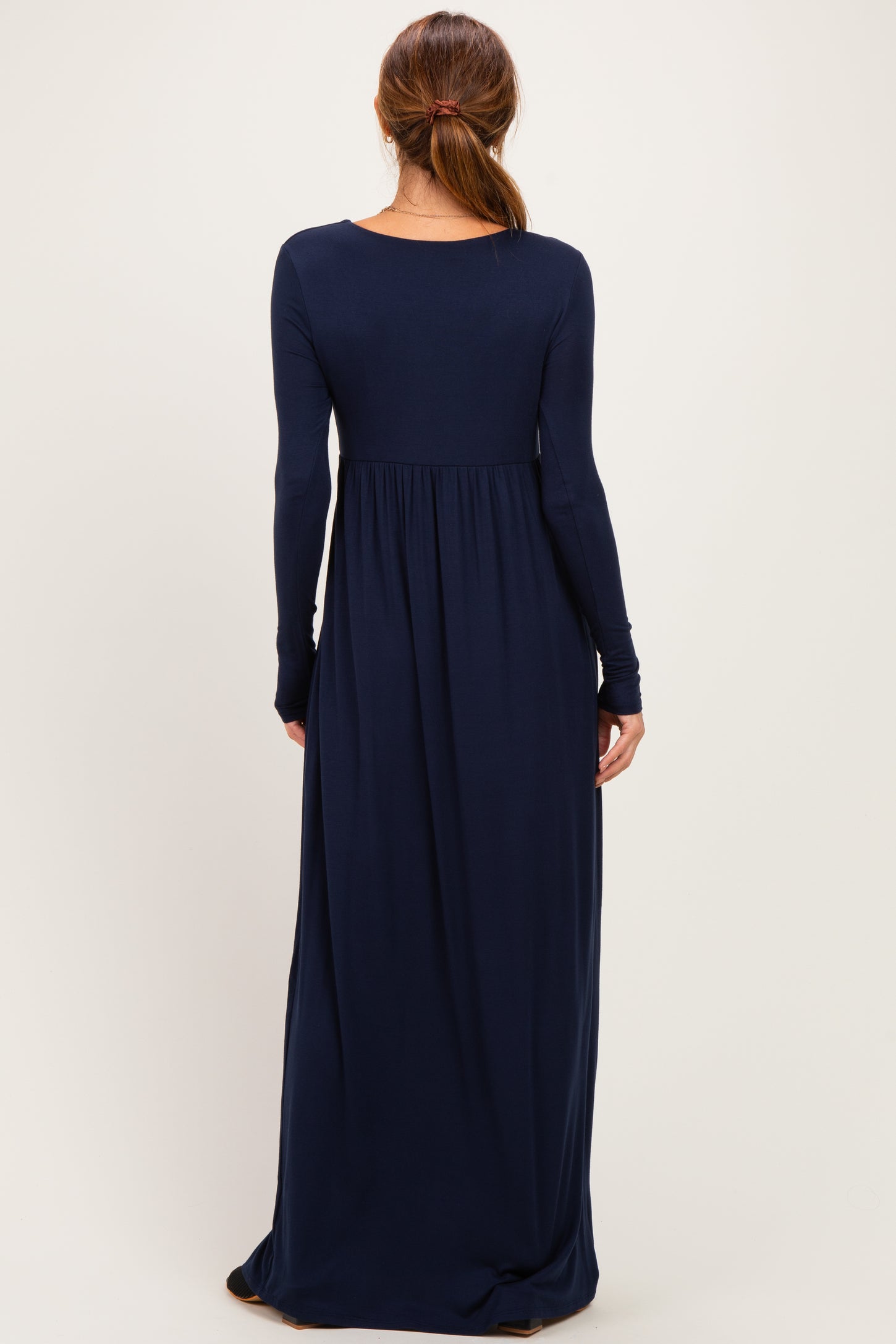 woman wearing a long navy blue maxi dress with long sleeves and a fitted bodice that flares out at the waist