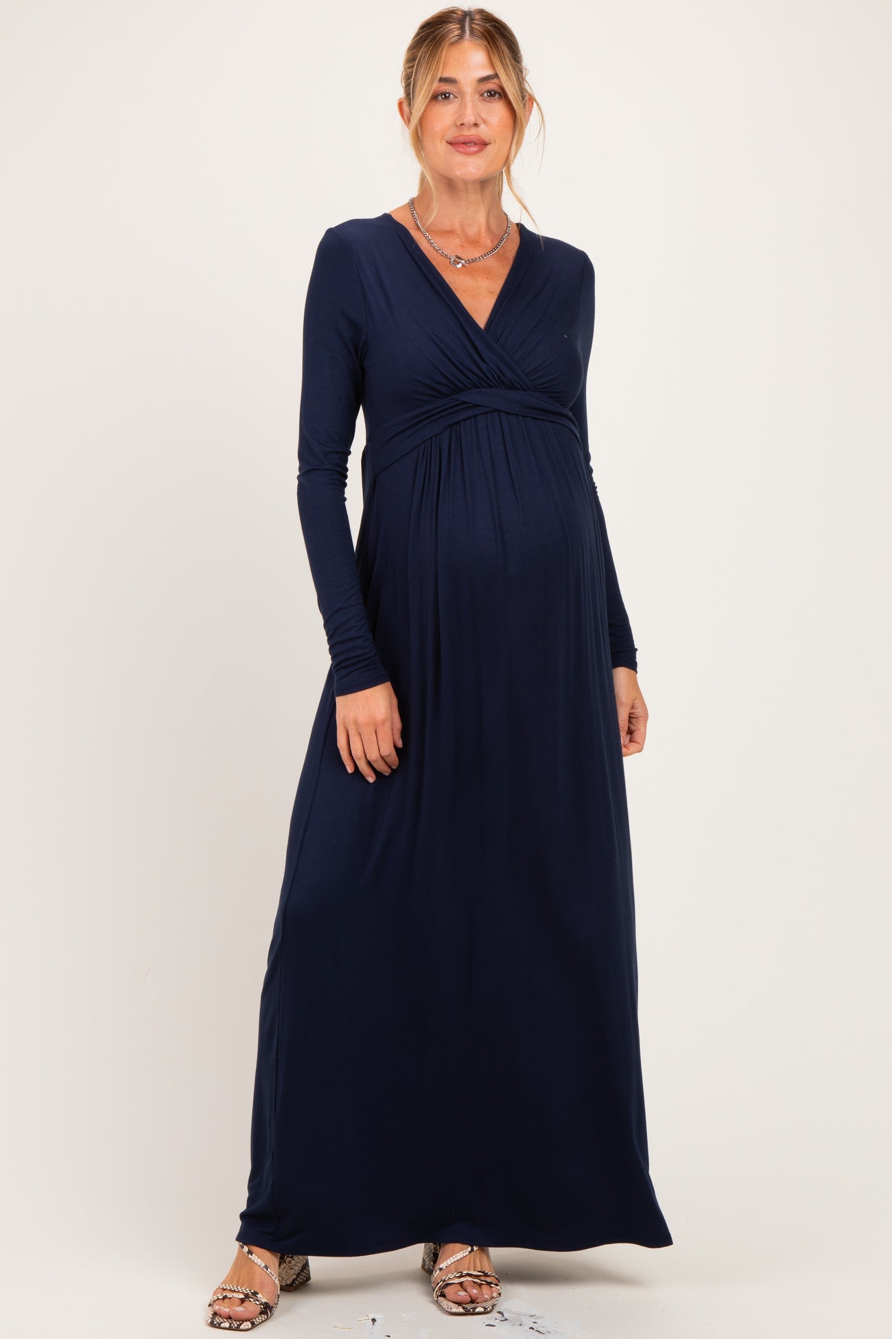 woman wearing a navy blue long sleeve maternity maxi dress with a fitted bodice and flowing skirt, showcasing her baby bump