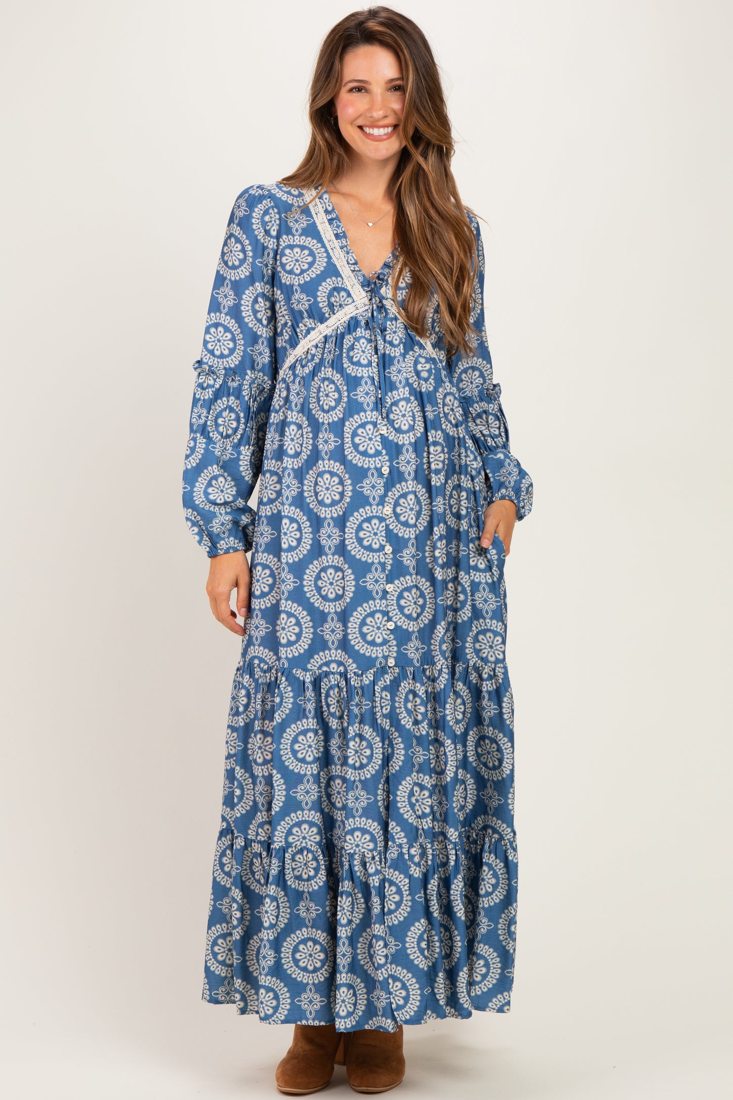 woman wearing a blue patterned maternity maxi dress with long sleeves and a tiered skirt, smiling at the camera