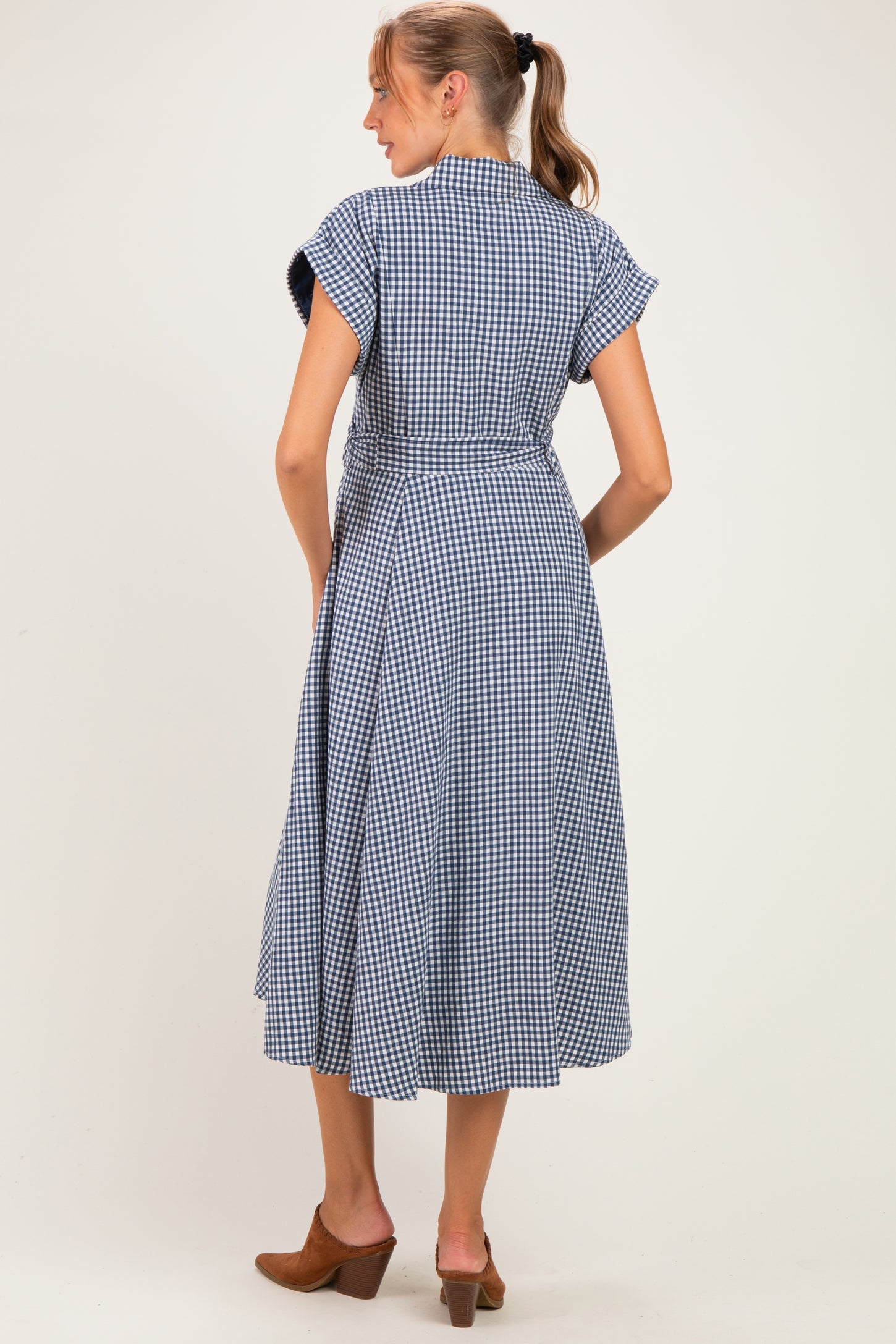woman wearing a navy and white gingham patterned maternity dress, showing the back view with cap sleeves and a tied waist