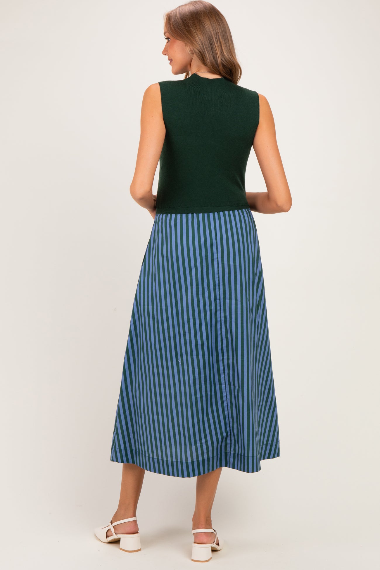 woman wearing a green sleeveless maternity dress with a blue striped skirt, showing a slight baby bump from the back