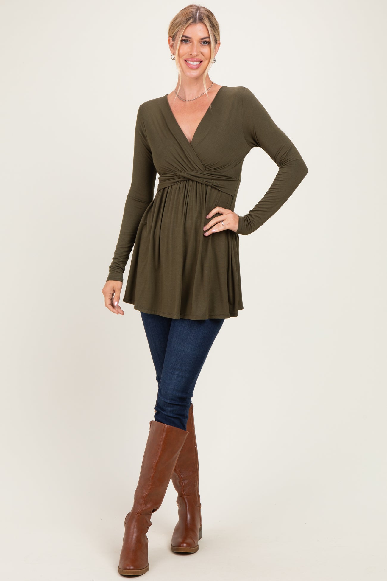 woman wearing an olive green long sleeve wrap top paired with dark jeans and brown knee-high boots