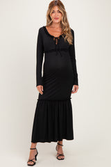 woman wearing a black long sleeve maternity dress with a tie detail and ruffled hem, showcasing her baby bump
