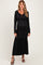 woman wearing a black long sleeve maternity dress with a tie detail and ruffled hem, showcasing her baby bump