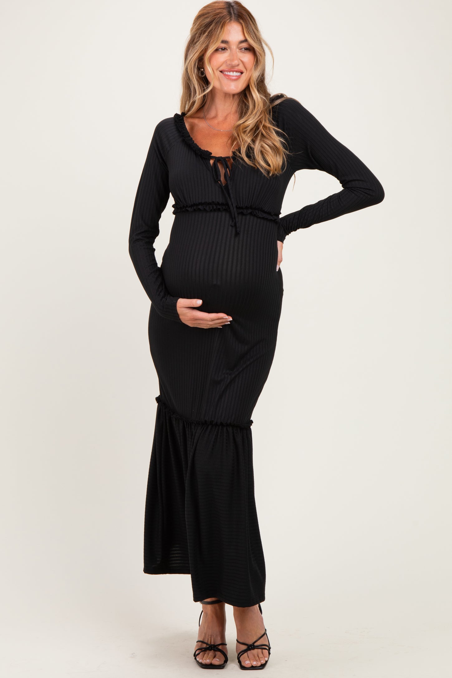 woman wearing a black ribbed maternity dress with long sleeves and a ruffled hem, showcasing her baby bump