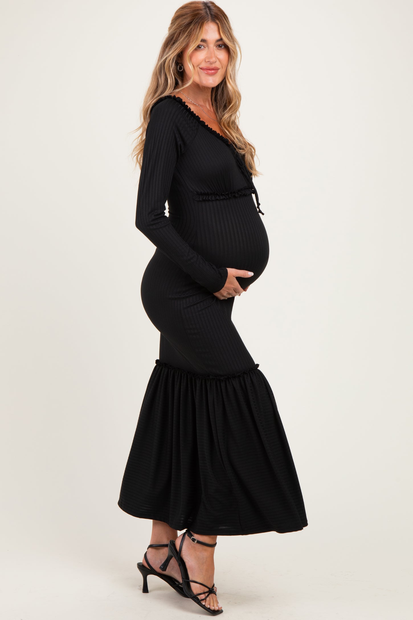 woman wearing a black ribbed maternity dress with ruffle details, holding her baby bump
