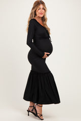 woman wearing a black ribbed maternity dress with ruffle details, holding her baby bump