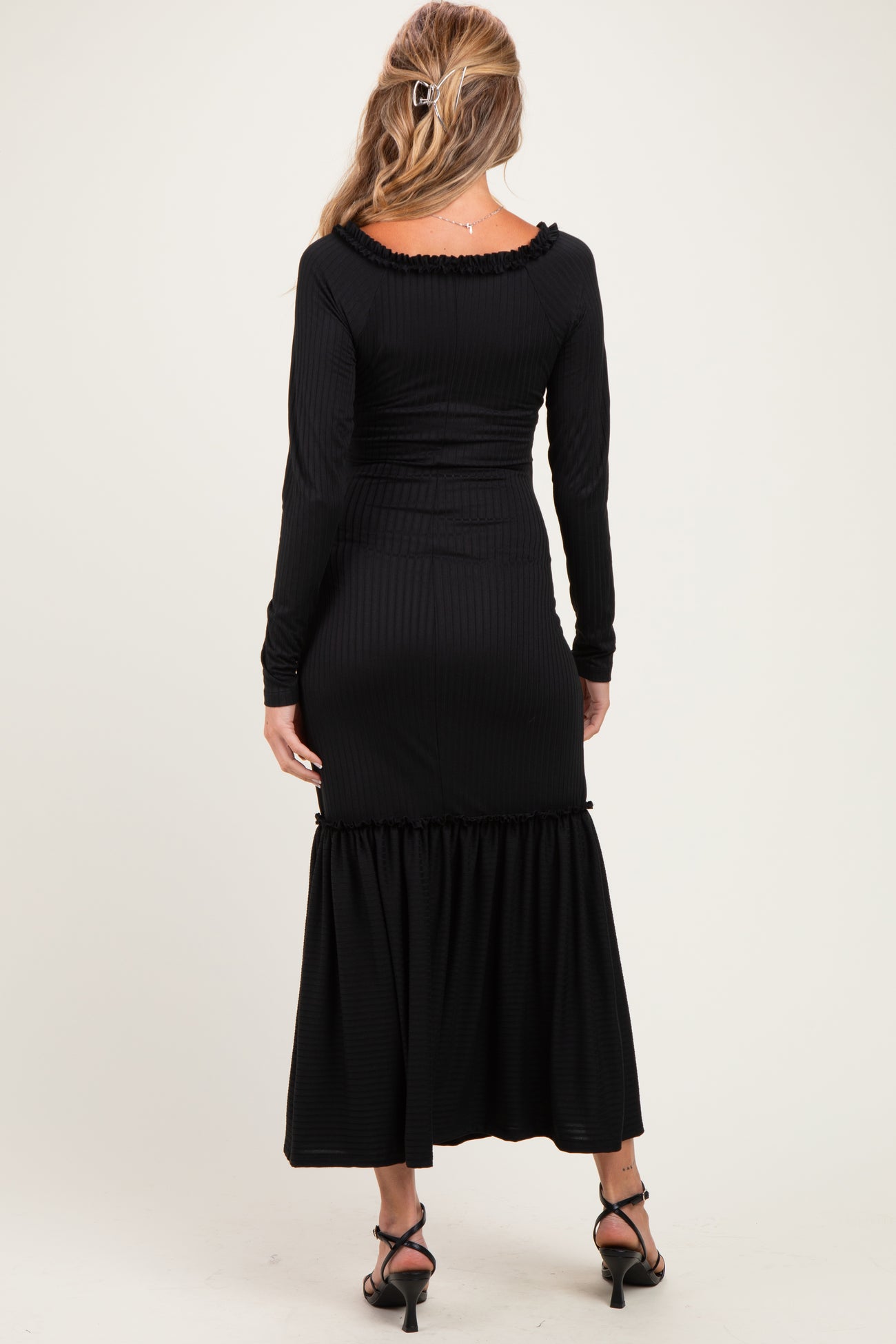 woman wearing a black ribbed maternity maxi dress with long sleeves and a ruffled hem, showing her back