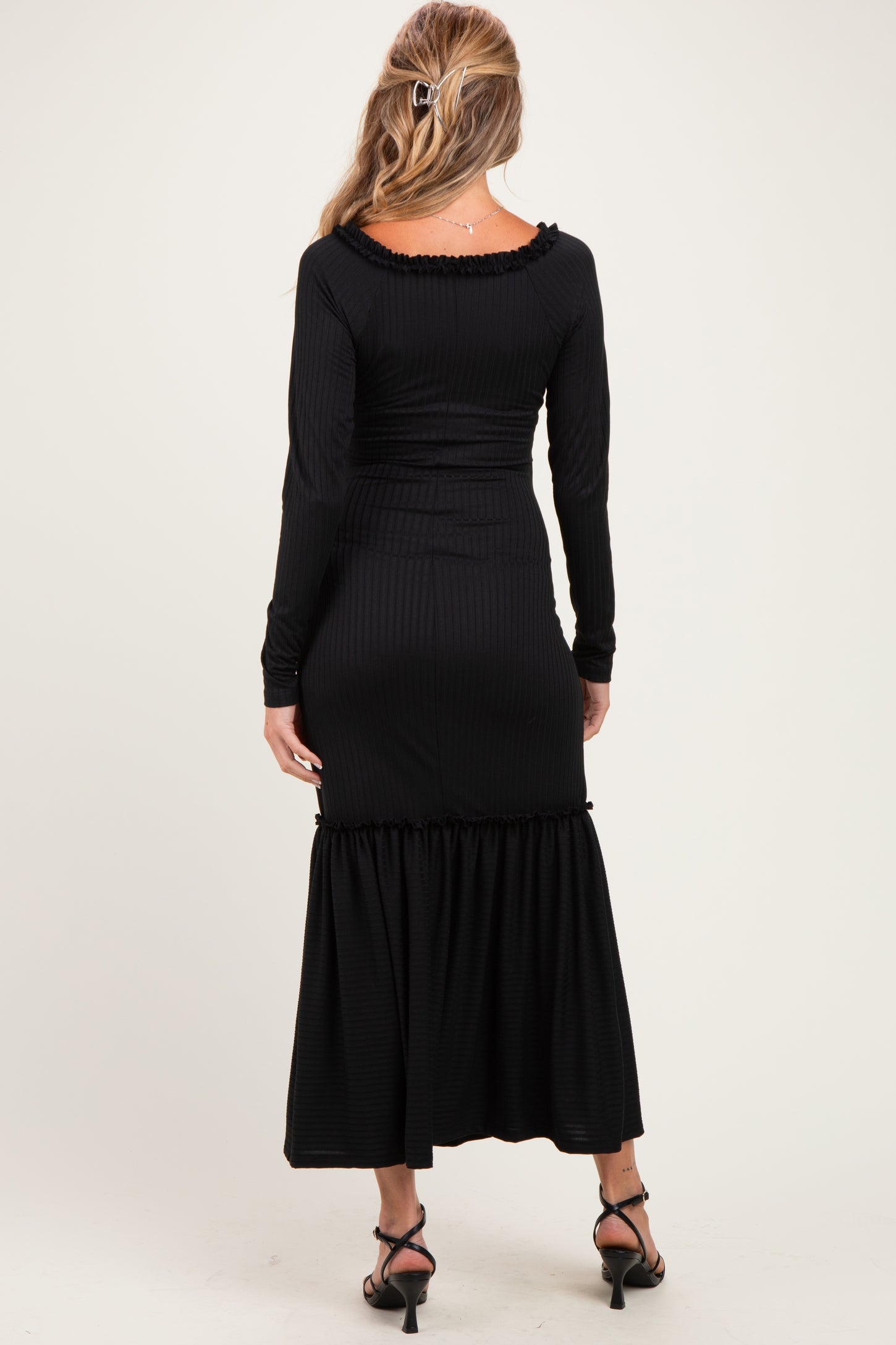 woman wearing a black ribbed maternity maxi dress with long sleeves and a ruffled hem, showing her back