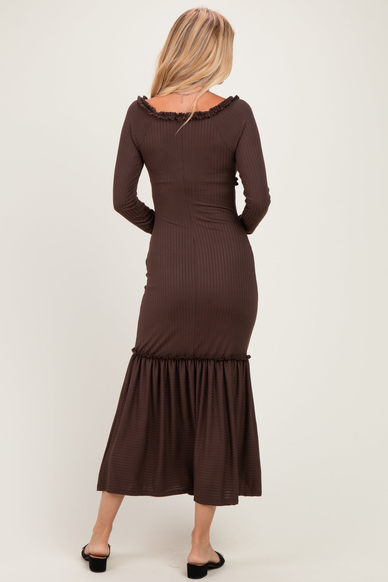woman wearing a chocolate brown ribbed long sleeve maxi dress with a ruffled hem, viewed from the back