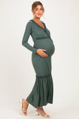 woman wearing a dark green long sleeve maternity dress with a gathered hem and holding her baby bump