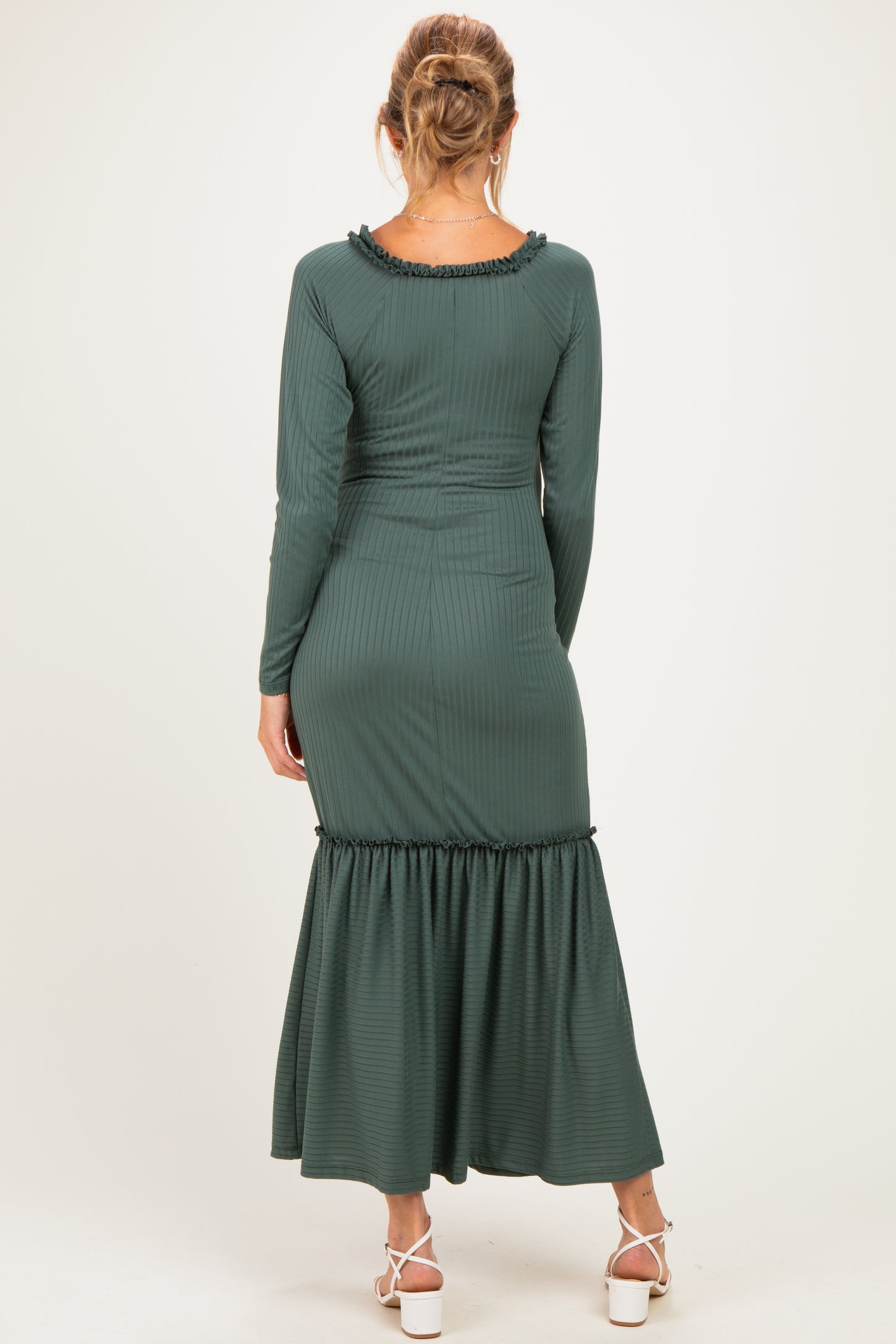 woman wearing a dark green long sleeve maternity dress with a ruffled hem and textured fabric, facing away from the camera